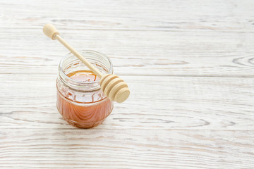 Jar of honey with honey stick on white wooden background. Selective focus. Copy space composition