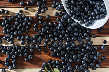 Bowl full of aronia spilled on wooden table