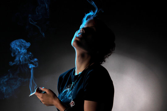 Eine Frau raucht eine Zigarette in Dunkelheit und der blaue Rauch leuchtet