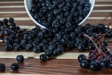 Bowl full of aronia spilled on wooden table