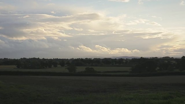 Dark rural autumnal landscape with brown mowed wheat field, Tarvin, Cheshire, England, UK. Overcast sky with mountains and hills in background. Sunset sky