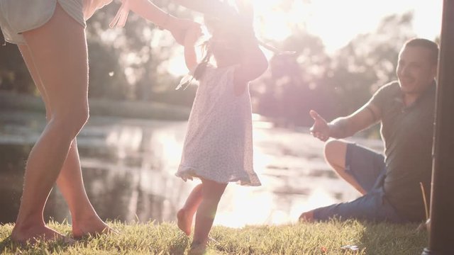 Little baby learns to walk. First Steps. Slow Motion 120 fps, 4K. Parents are teaching their child to do the first steps on a green grass in summer. Happy childhood and Parenthood concept. Family love