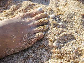 Women's foot with painted silver fingernails. Leg standing on the sand. Pedicure