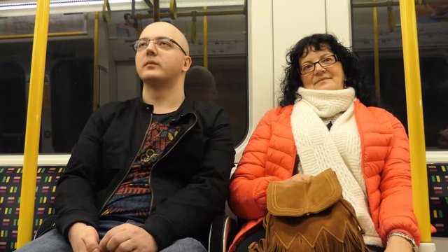 Couple, man and woman both wearing glasses sitting inside subway metro underground or tube moving train car