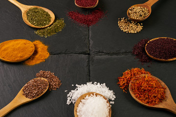 Colorful indian spices in wooden spoons on dark stone background