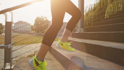 Woman feet jogging up stairs, close up. Steadicam stabilized shot. Slow Motion. Sportswoman wearing barefoot sports shoes while training on the sunny stairs. Lens Flare.