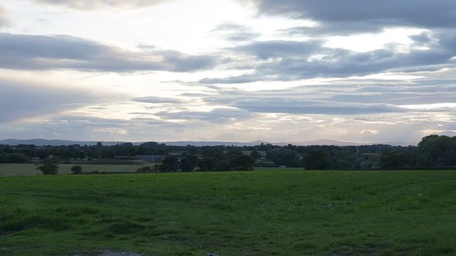 Rural landscape with green grass meadow, Tarvin, Cheshire, England, UK. Overcast sky with mountains and hills in background.