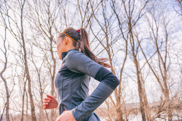 Running woman in autumn forest outdoors in morning fresh air doing cardio workout exercise living a healthy lifestyle. Girl runner in sport jacket training in cold fall season.