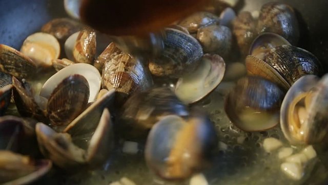 Close up of delicious clams opening their shells cooked for a tasty seafood stir fry meal. Stewing mussels in a black frying pan on a hot plate.