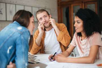 Portrait of young group of people working together in office. Young man talking on his cellphone and happily looking aside while two beautiful girls sitting in classroom and talking