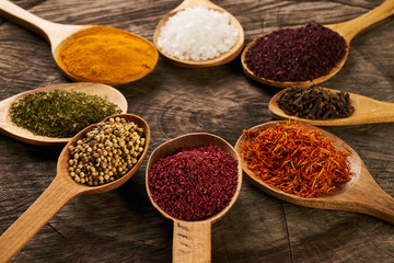 Colorful spices in wooden spoons on dark wooden background