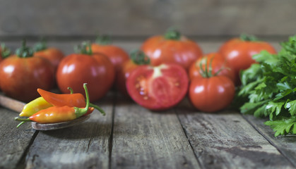 Chilli peppers in wooden spoon with tomatoes and parsley in background. selective focus