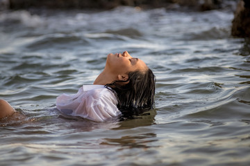 Fototapeta premium Chica joven con camisa blanca tumbada en el agua del mar al atardecer.