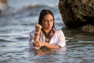 Fototapeta premium Chica joven con camisa blanca bañándose en el mar al atardecer y colocandose la camisa.