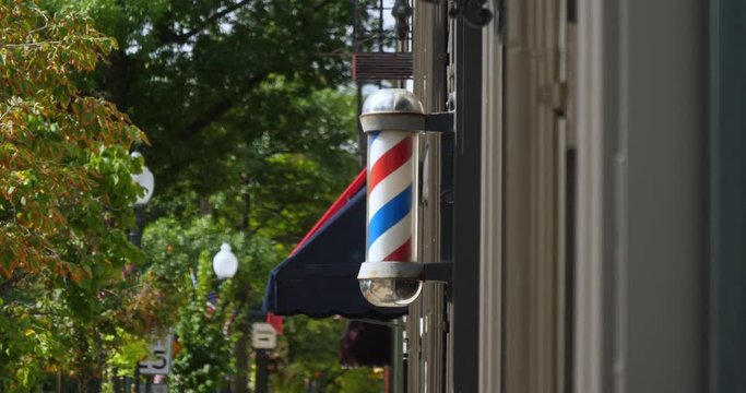 A daytime exterior view of a spinning barber pole outside an establishment in a small town.  	