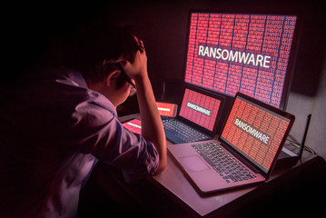 Young Asian male frustrated, confused and headache by ransomware attack on desktop screen, notebook and smartphone, cyber attack and internet security concepts - 171000650