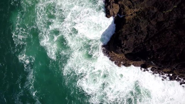 Aerial rising top down view of breaking waves along rocky ocean shore