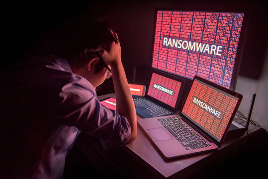 Young Asian male frustrated, confused and headache by ransomware attack on desktop screen, notebook and smartphone, cyber attack and internet security concepts