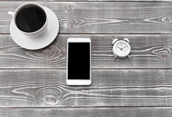 Naklejka premium a cup of coffee, a smartphone, an alarm clock on a wooden background.