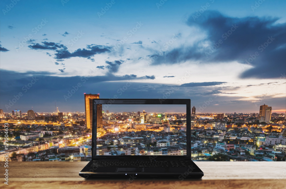 Poster computer laptop on wooden table with bangkok city view in dusk. clipping path computer screen