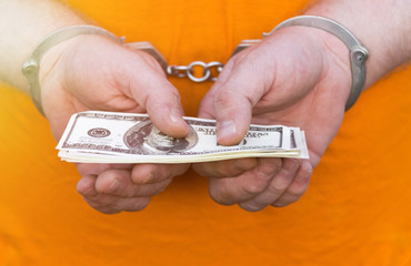 Hands in handcuffs hold a bundle of dollar bills. man in an orange T-shirt. corruption.