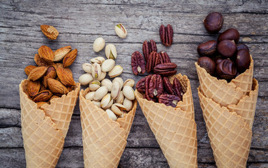 Concept for homemade various nuts ice cream. Mixed nuts in waffle cones on shabby wooden background.top view