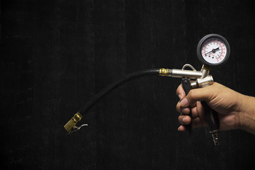 Hand holding an inflator gauge tools, Hand of mechanic man checking air pressure gauge of car tyre with black painted cement wall background with copy space for writing text, Automotive parts concept.