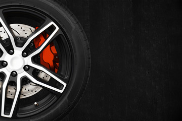 Alloy wheels of racing car with metal brake discs and red caliper on a black cement wall background with copy space your writing text on the right. Automotive parts concept. - obrazy, fototapety, plakaty