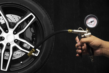 Hand holding an inflator gauge tools, Alloy wheel of racing car and metal brake disc with black caliper, Hand of mechanic man checking air pressure gauge of car tyre with black cement wall background.
