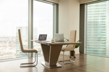 Image of work desk with two laptops on it and comfortable armchairs beside in bright office...