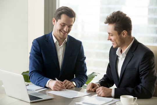 Happy smiling businessman signing contract with satisfied business partner, accepting terms of agreement, making good deal with perspective company. Investor approving financing of interesting project