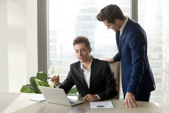 Employee sitting at workplace and explaining interesting idea to his boss. Executive manager standing near desk and listening proposal of economist about improving company efficiency and profitability