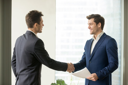 Handsome businessman handshaking with company coworker or partner at meeting, employer welcoming job candidate before interview. Business etiquette, entrepreneurs partnership, making successful deal