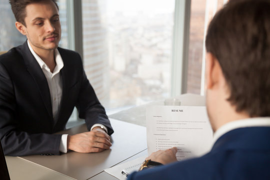 Back view of hiring manager pointing on clauses in resume and asking job applicant questions. Employer conducting interview with candidate, specifying work experience. Close up image, focus on resume