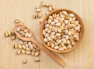 Wooden bowl with pistachios and wooden spoon on the bamboo background.