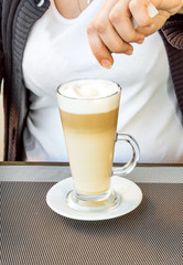 A woman pours sugar in a latte.