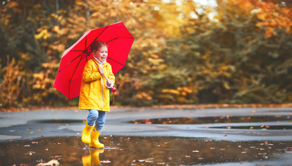 happy child girl with an umbrella and rubber boots in puddle  on autumn walk