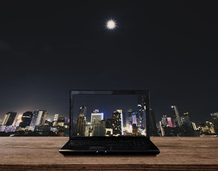 Computer laptop on wooden table with modern buildings in the city background. Clipping path computer screen