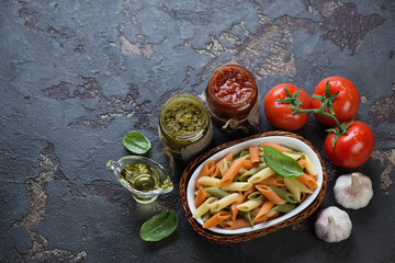 Boiled three-colored penne pasta with different pesto sauces, horizontal shot with space on a brown stone background, above view