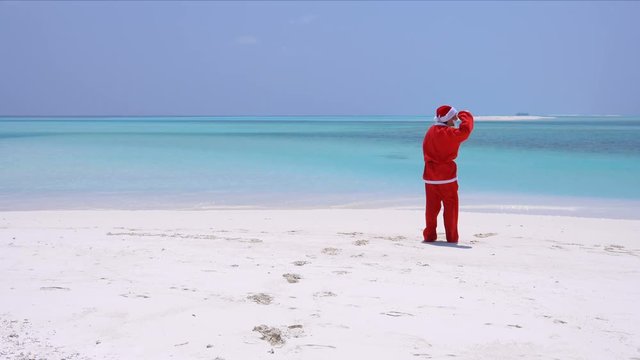 Man in Santa Claus Hat running and jumping along the beach. Christmas vacation on Maldivian islands