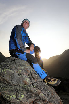 Good-looking young hiker taking a break on a stone and enjoys the sunrise in the swiss mountains