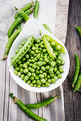 Green pea in white  bowl on rustic wooden table, top view