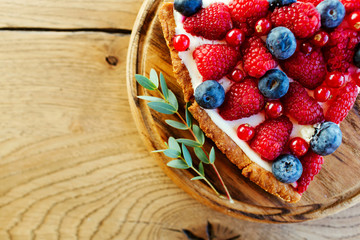 A piece of berry tart with raspberries and blueberries on wooden background with copy space