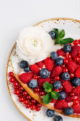 Berry tart with raspberries and blueberries decorated with flowers and mint