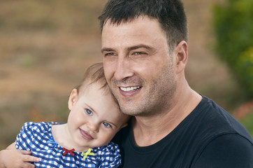 Father is holding his beautiful baby with eyes blue. Father and daughter playing outdoors. Smiling