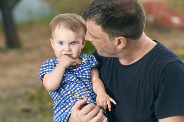 Father is holding his beautiful baby with eyes blue. Father and daughter playing outdoors