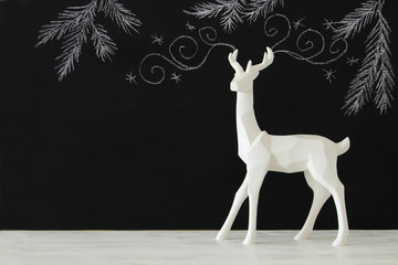 White reindeer on wooden table over chalkboard background whith hand drawn chalk illustrations