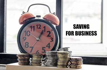 Clock and coins with the word SAVING FOR BUSINESS - the concept of savings