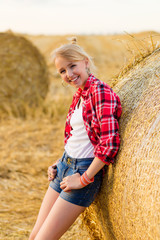 Naklejka na ściany i meble Young girl on straw sheaves in a field