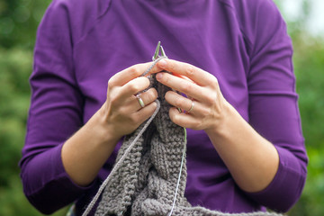 Close-up A young cheerful woman in a purple sweater knits with knitted needles of a natural Italian wool cardigan